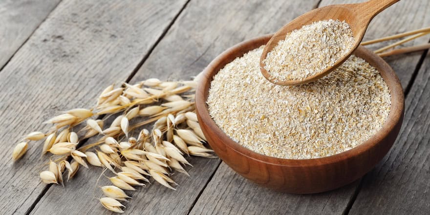 oat bran in bowl and in spoon with dry ears near on wooden table son avoine